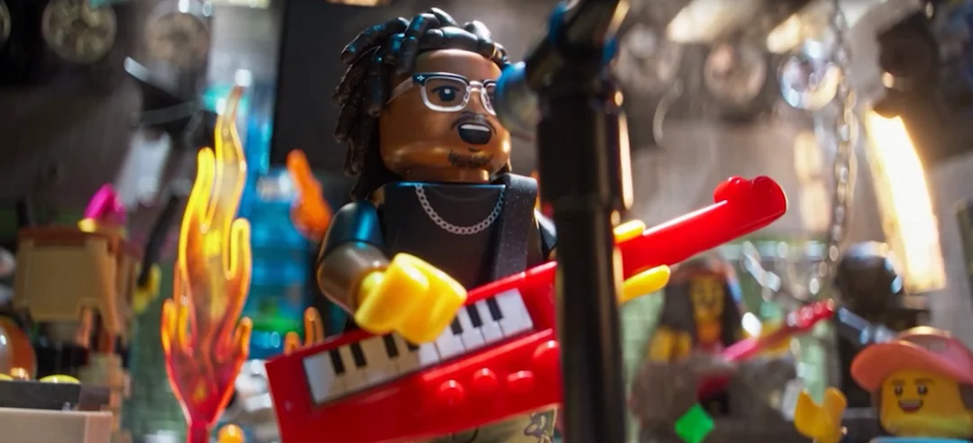 Close on the same minifigure — dreadlocks, glasses, chain — playing the red keytar beside a moulded flame