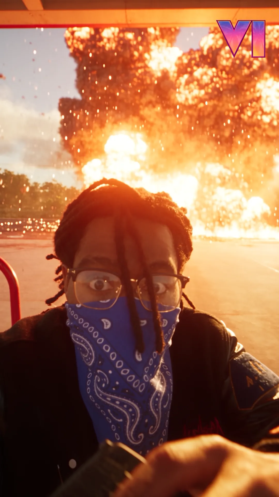A man wearing a blue bandana over his face films himself as a huge orange fireball erupts across the road behind him